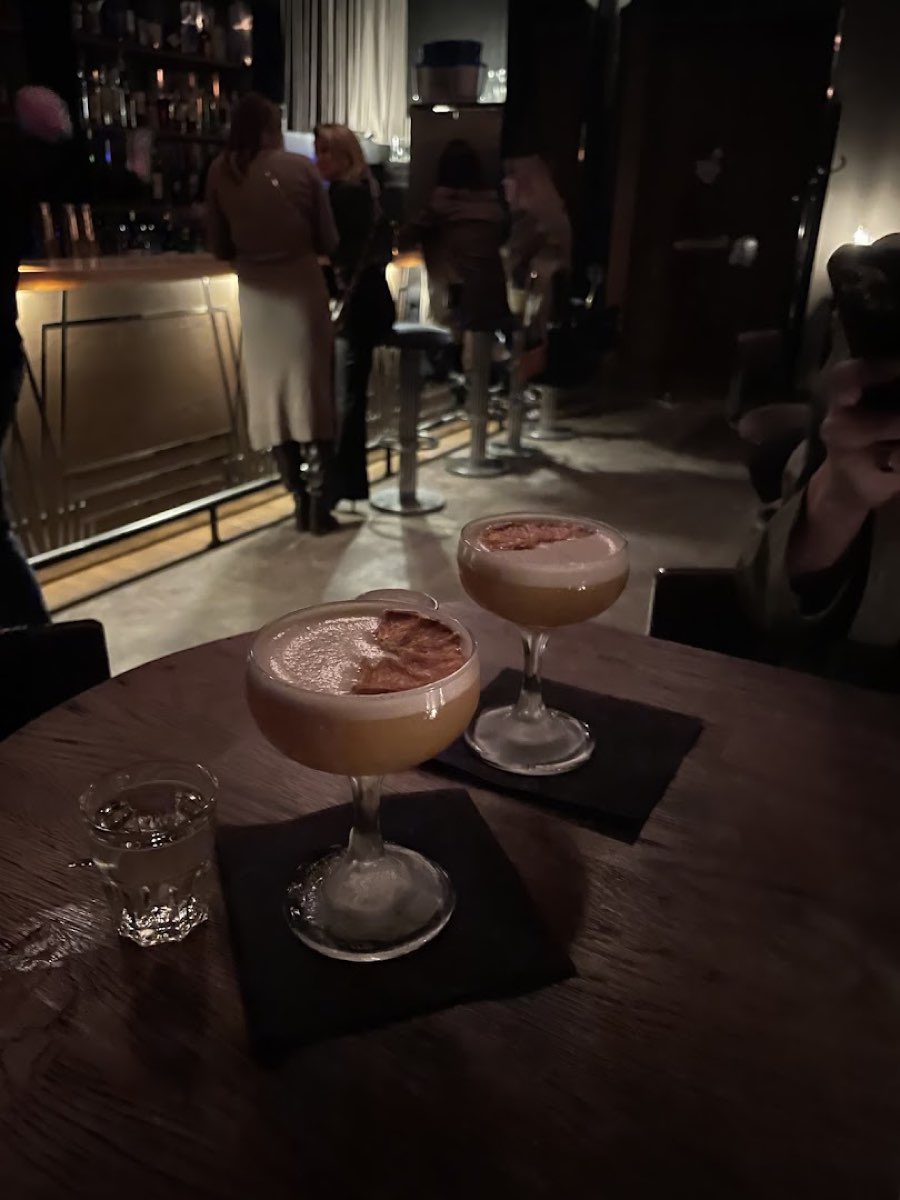 Dwa koktajle coupe z aksamitną pianką na ciemnym drewnianym stole przy świecach