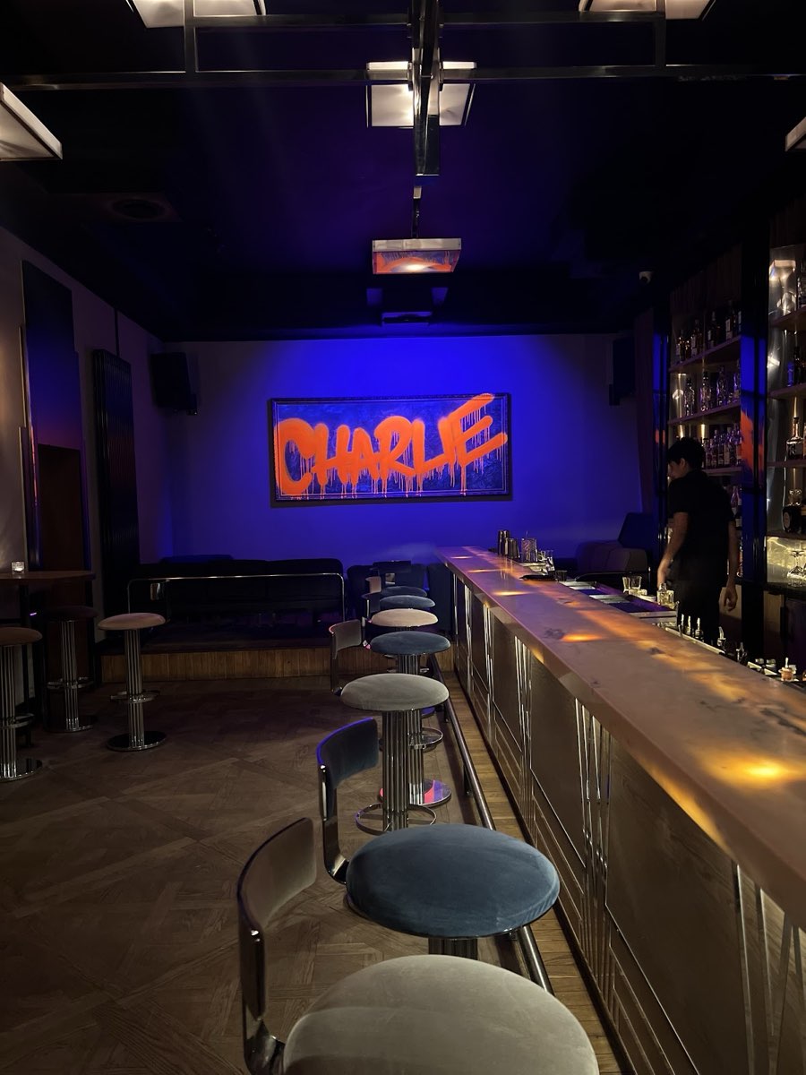 Niebiesko podświetlona sala z podświetlanym napisem CHARLIE nad długim barem w salonie lokalu