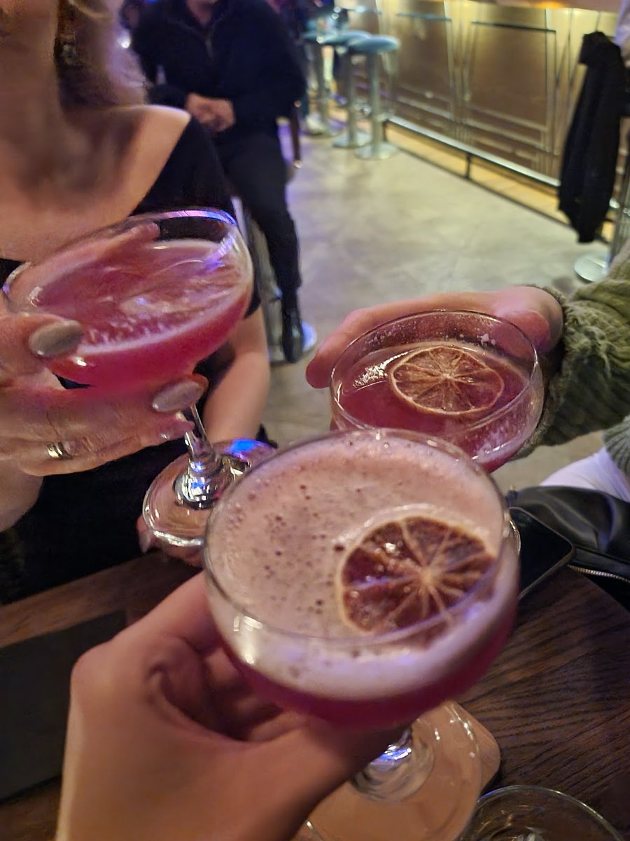 Trzy różowe koktajle coupe wznoszone do toastu przy barze CHARLIE